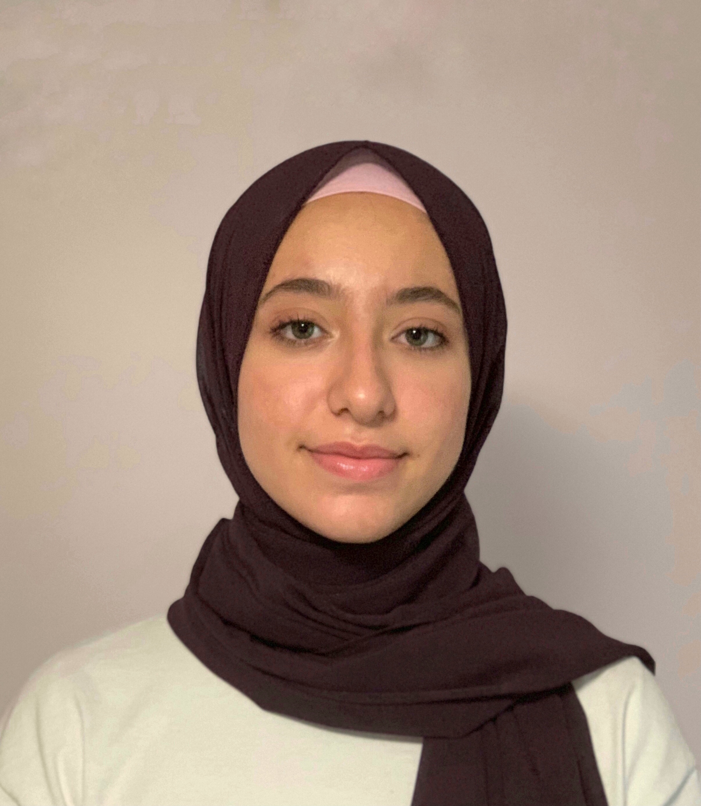 Leena Alzafarani Portrait of a smiling person wearing a brown hijab against a neutral background.